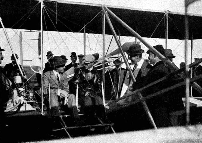 Illustration:
Wilbur Wright erklärt dem neben ihm sitzenden König von Spanien seine
Flugmaschine.
